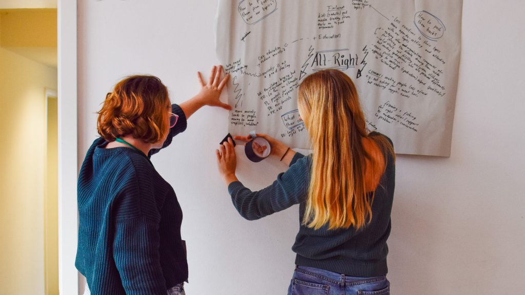 Photograph showing two women taping a flipchart page to a wall.